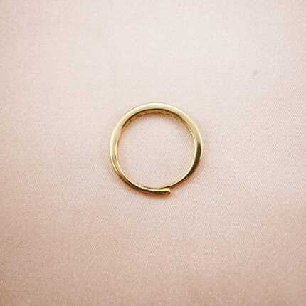 Minimalist peridot ring with a gold-tone band displayed on a soft fabric background.