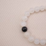 Close-up detail of the moonstone bracelet showing the glossy black obsidian bead.