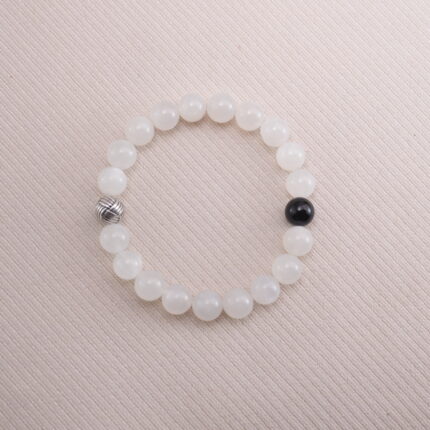White moonstone beaded bracelet with a single black obsidian accent bead, displayed on a soft beige background.