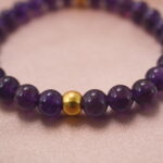 Close-up of deep amethyst bracelet showing clear crystal texture and polished gold bead.