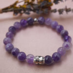 Lifestyle photo of amethyst bracelet with silver accent, placed on soft pink fabric for a peaceful mood.