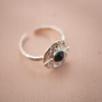 Side view of silver evil eye adjustable ring highlighting its open band and obsidian gemstone.