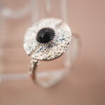 Lifestyle image of silver evil eye adjustable ring with obsidian gemstone, styled on a soft beige background.