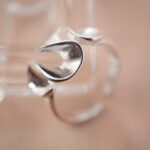 Lifestyle image of silver petal open ring styled on a warm beige background.