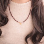 A model wearing a slender garnet beaded necklace with small amethyst and colored gemstone accents.