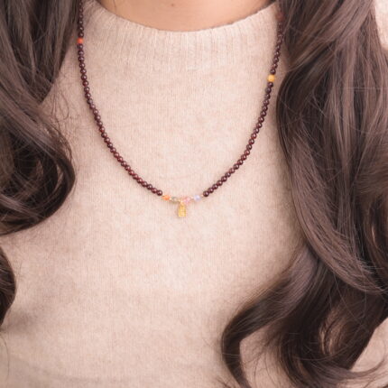 A model wearing a slender garnet beaded necklace with small amethyst and colored gemstone accents.