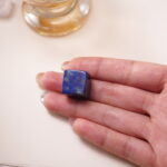 Lapis lazuli crystal cube in hand, vibrant blue with golden flecks, promoting clarity and truth.