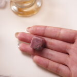 Rhodonite crystal cube in hand, radiating gentle pink energy for emotional healing and compassion.