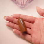 Tiger’s eye crystal point in hand, shimmering with golden-brown bands that symbolize strength and courage.