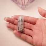 Tourmalinated quartz crystal point held in hand, featuring clear quartz with natural black tourmaline inclusions.