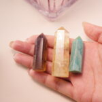 Three crystal points held in hand – smoky quartz, citrine, and amazonite – radiating bright, uplifting energy.