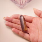 Smoky quartz crystal point in hand, with deep brown clarity representing grounding and protection.