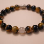 Close-up detail of tiger’s eye and white chalcedony bracelet featuring a silver fish bead, showing the smooth polish, reflective surface, and delicate carved details.1