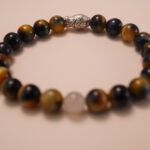 Close-up detail of tiger’s eye and white chalcedony bracelet featuring a silver fish bead, showing the smooth polish, reflective surface, and delicate carved details.2