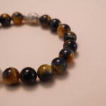 Close-up detail of tiger’s eye and white chalcedony bracelet featuring a silver fish bead, showing the smooth polish, reflective surface, and delicate carved details.3