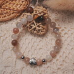 Rainbow moonstone and tiger’s eye bracelet with a silver “I love you” heart accent displayed in a natural lifestyle setting under daylight, capturing the balance between glowing moonstone and warm tiger’s eye tones.