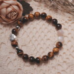Tiger’s eye and moonstone bracelet with a silver heart bead displayed in a natural lifestyle setting under daylight, emphasizing the harmony of golden tiger’s eye and iridescent moonstone.