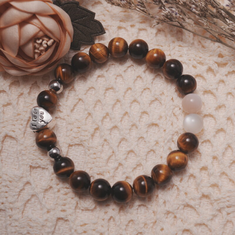 Tiger’s eye and moonstone bracelet with a silver heart bead displayed in a natural lifestyle setting under daylight, emphasizing the harmony of golden tiger’s eye and iridescent moonstone.