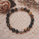 Tiger’s eye and white chalcedony bracelet with a silver fish bead displayed in a natural lifestyle setting on a soft textured fabric, highlighting its warm golden shimmer and symbolic fish charm.