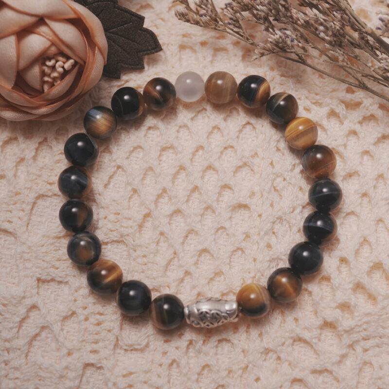 Tiger’s eye and white chalcedony bracelet with a silver fish bead displayed in a natural lifestyle setting on a soft textured fabric, highlighting its warm golden shimmer and symbolic fish charm.